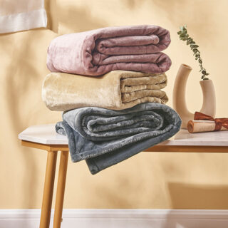 pile de trois plaid pliés, un rose sur un jaune sur un gris, sur une table basse en bois, à côté d'un vase et d'un parchemin, dans une pièce avec un mur jaune